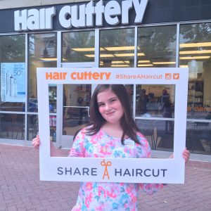 Young girl posing with share a haircut frame in front of salon