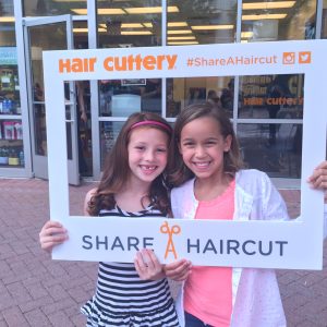 two young girls pose holding share a haircut frame