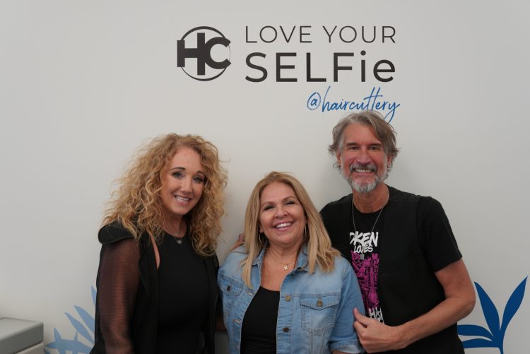 Hair Cuttery team members smiling in front of wall art that says 'Love your selfie'.